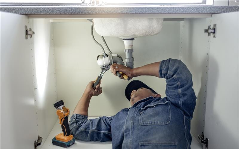 Plumber repairing pipes beneath a bathroom sink in Rialto