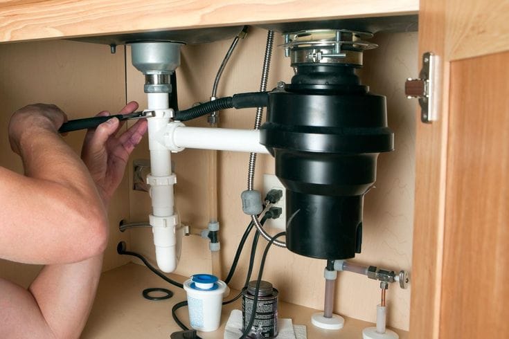 Plumber installing a garbage disposal beneath a kitchen sink in Rialto