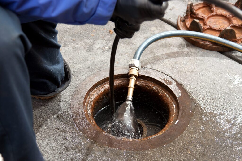 Plumber hydro jetting a sewer line through a manhole in Rialto