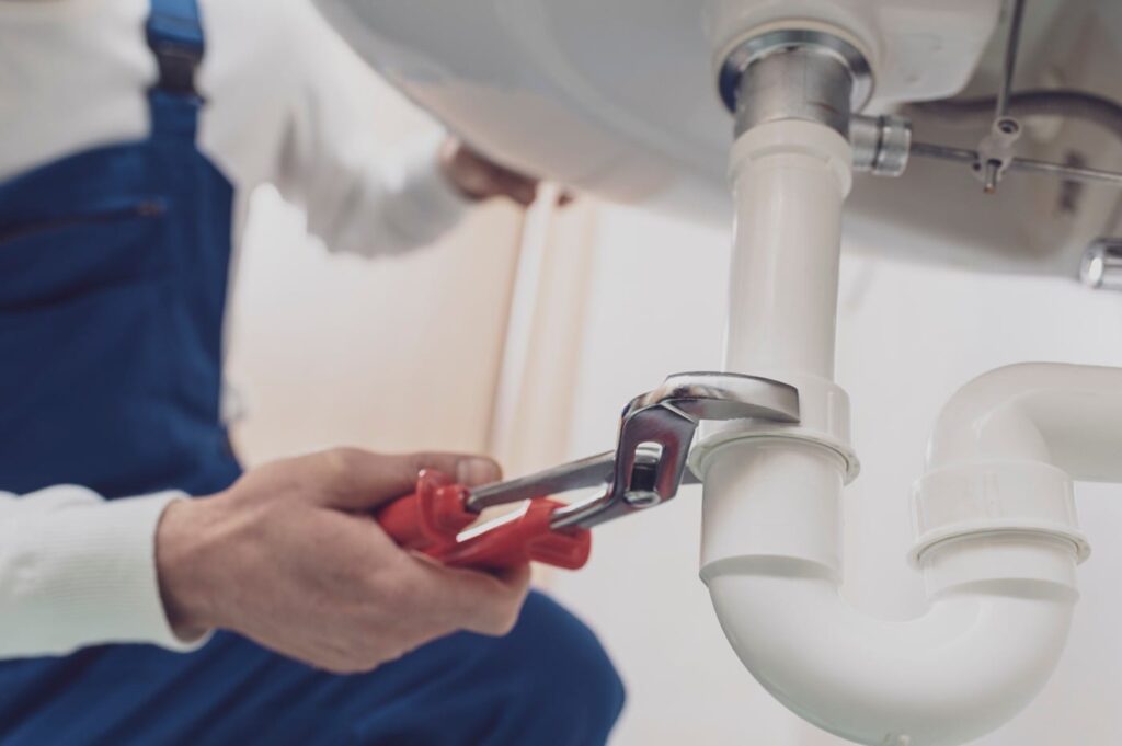 Plumber repairing a white drain pipe beneath a sink in Rialto