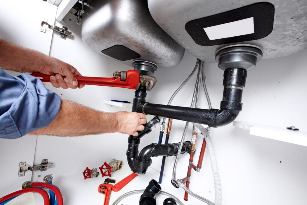 Plumber repairing drain pipes beneath a kitchen sink in Rialto